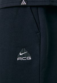 Dunkelblaue Sportshorts aus weichem Stoff, mit lockerer Passform, seitlichen Taschen und einem gestickten ACG-Logo in Weiß und Hellgrau.