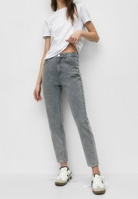 Szare jeansy o wysokim stanie w slim fit z przetarciami, w połączeniu z białą koszulką z okrągłym dekoltem i casualowymi białymi sneakersami.