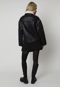 Sort faux læderjakke med en hyggelig hvid shearlingkrave, der har en afslappet pasform og synlige syninger på ryggen.