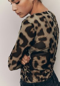 Top lungo a maniche trasparenti con stampa leopardata e dettaglio arricciato sul lato. Caratterizzato da una texture liscia e una silhouette aderente, in toni naturali.