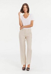 Un pantalon large beige avec des poches avant et une fermeture à bouton, associé à un T-shirt blanc à col en V et des talons plateformes noirs.