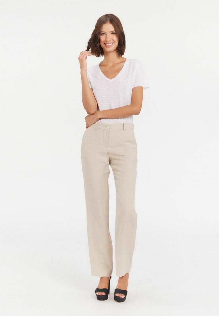 Un pantalon large beige avec des poches avant et une fermeture à bouton, associé à un T-shirt blanc à col en V et des talons plateformes noirs.