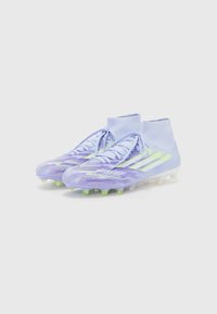 Purple soccer cleats with a textured design, featuring green accents and a sock-like collar, laces, and molded studs for traction.