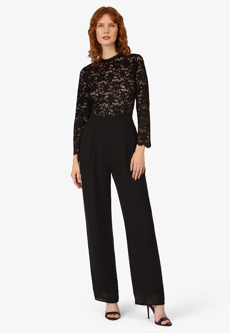 Czarny kombinezon z dopasowanym koronkowym gorsetem i długimi rękawami, z szerokimi nogawkami i gładką teksturą. Posiada akcentowany wysoki dekolt.