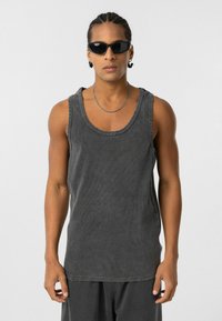Grijze mouwloze tanktop met een geribbelde textuur, voorzien van een ronde halslijn en een rauw afgewerkte onderzijde. Gekozen in combinatie met zwarte zonnebril en een zilveren ketting.
