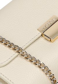 Krémová kožená kabelka s texturovaným povrchem, vybavená zlatým kovovým uzávěrem a ozdobným řetízkovým popruhem.