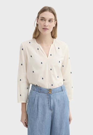 Blusa color crema con motivos de árboles en azul marino, escote en v y mangas largas, combinada con pantalones de talle alto en azul claro con dos botones.