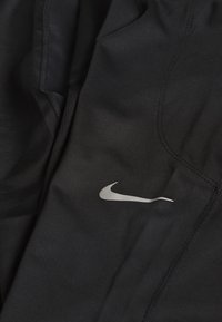 Czarne sportowe spodenki z gładkiego materiału, z srebrnym logo Nike po lewej stronie, z widocznymi szwami i eleganckim designem.