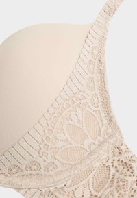 Beige bh met gladde, padded cups en kantdetails langs de randen, met een gestructureerde band met een verfijnd patroon.