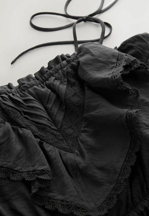 Čierna blúzka s volánmi, textúrovanou látkou a plisovaním, doplnená čipkovými detailmi. Sťahovanie na krku pre nastaviteľné prispôsobenie.