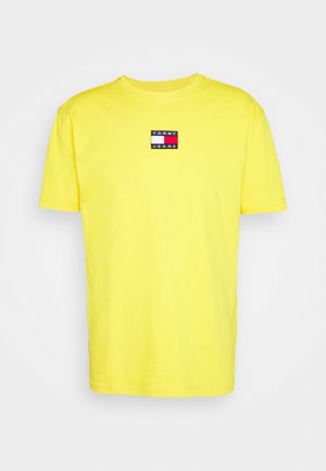 Kurzärmliges gelbes T-Shirt aus Baumwolle, mit einem rechteckigen gestickten Aufnäher mit "TOMMY JEANS" in Schwarz, Rot und Weiß.