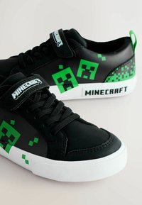 Zapatillas sintéticas negras con parte superior texturizada, gráficos pixelados verdes de Minecraft y suela de goma blanca con el logotipo.