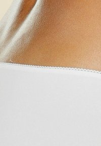 Tissu blanc lisse avec un bord festonné, mettant en avant un gros plan d'une teinte de peau, soulignant la texture et le design.