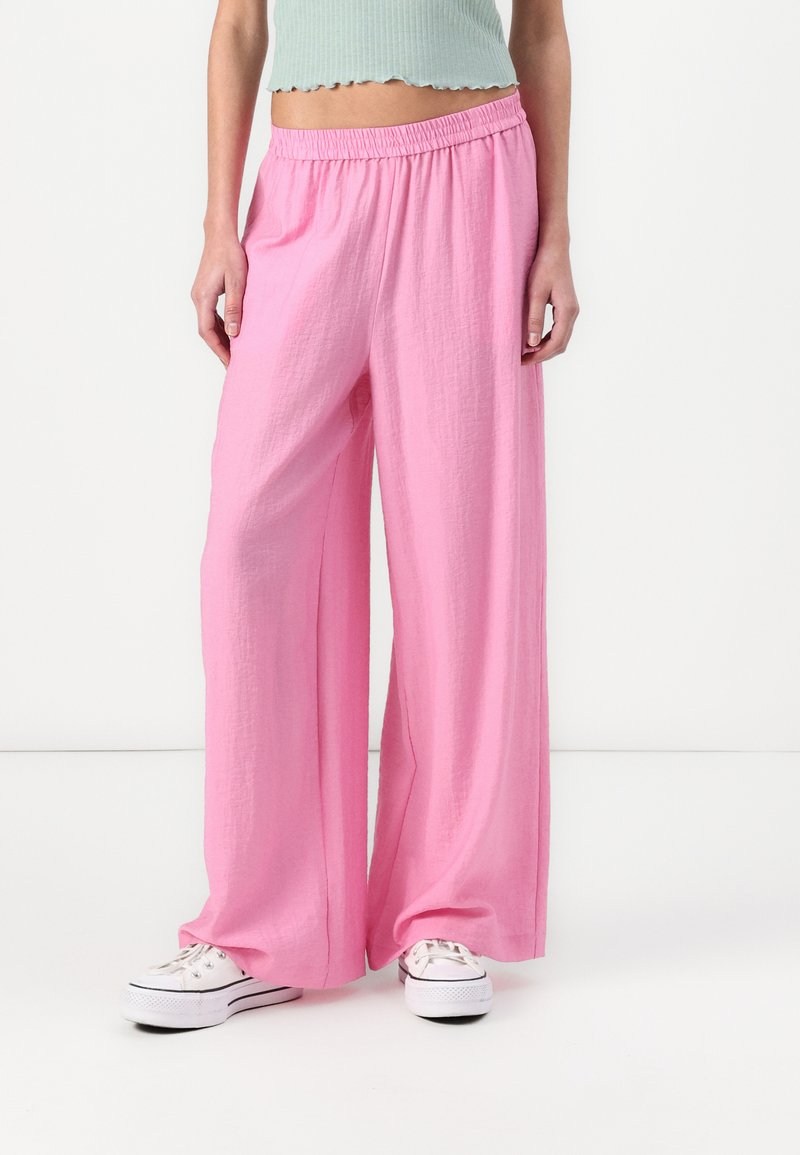Pantaloni rosa leggeri a gamba larga con un tessuto testurizzato e una vita elasticizzata, abbinati a sneaker bianche.