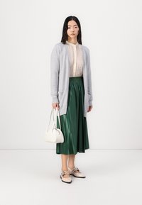 Lys grå cardigan, blondebluse, grøn plisseret midi-nederdel, beige flade sko med remdetaljer og en hvid håndtaske. Minimalistisk design.
