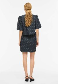 Tenue en denim comprenant un haut bleu foncé à manches bouffantes et une jupe assortie, toutes deux ornées de pois bleu clair.