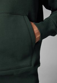 Dark green sweatshirt with a kangaroo pocket, ribbed cuffs, and a smooth texture. Features contrast stitching along the seams.
