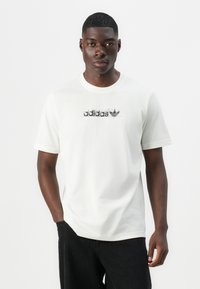 White cotton t-shirt with short sleeves, featuring a black printed logo across the chest. Relaxed fit with a round neckline.