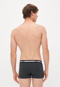 Boxer ajustados negros con un patrón geométrico, cinturilla elástica etiquetada "HUGO" y un diseño ceñido. Tela suave con estiramiento mínimo.