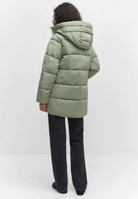 Mintgrüne Steppjacke mit Kapuze, mit gesteppten Partien und einem lockeren Schnitt. Kombiniert mit dunklen Jeans, die eine legere Silhouette zeigen.