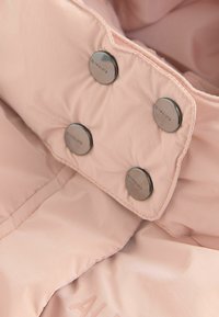 Giacca rosa chiaro con una texture in nylon liscia, dotata di bottoni a pressione argentati e un discreto logo del brand impressa sul tessuto.