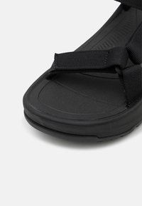 Mustat sandaalit, joissa on kuvioitu kumipohja, leveät punotut remmit ja pehmustettu pohjallinen mukavuuden ja vakauden takaamiseksi.