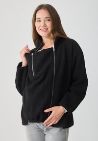 Čierna fleecová bunda s vysokým golierom, zipsom na prednej strane a voľným strihom. Výrazná textura a dve postranné vrecká na zips. Mäkký a teplý materiál.