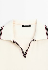 Ribbade krämfärgade polo-tröjan med djup V-krage och vit krage med mörkröda och marinblå ränder. Etiketten säger "Massimo Dutti."
