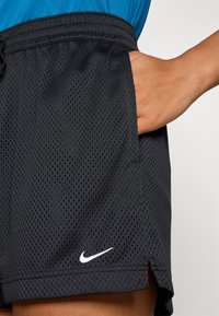 Sorte mesh treningsshorts med pustende tekstur, elastisk midje, sidelomme, og en hvit Nike-logo sydd på nedre venstre side.