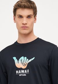 Czarna koszulka z długim rękawem wykonana z miękkiego materiału, z kolorowym graficznym znakiem ręki. Biały tekst "HAWAII" oraz "RIP CURL" poniżej wzoru.