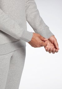 Grå sweatshirt med ribbade manschetter och nederkant. Mjukt, texturerat tyg som visar en närbild av händer som justerar manschetterna. Slät silhuett.