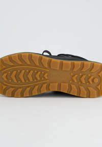 Sneaker noir avec une tige texturée, dotée d'une semelle extérieure en caoutchouc flexible de couleur tan contrastante, détaillée avec un motif de traction.