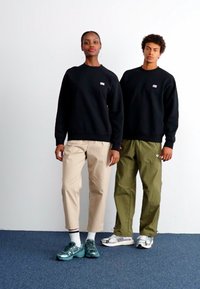 Mustad hallid kapuutsiga särgid, beežid kitsenevad püksid ja oliivrohelised kahepoolsed püksid. Peegeldavad sinised tennisekingad ja valged spordijalatsid. Lihtne disain logodega.