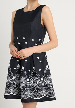 Navy ærmeløs kjole med tætsiddende liv og flared nederdel, med hvid blomsterbroderi og blonderkant ved kanten.