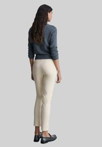 Grauer Strickpullover, enge cremefarbene Hose und schwarze Schuhe; Fokus auf Struktur und Farbkontrast; Modell von hinten gezeigt.