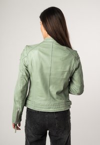 Giacca di pelle verde chiaro con un design aderente, caratterizzata da un colletto alto e polsini con zip. Texture liscia con sottili dettagli sulle spalle.