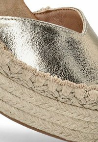 Espadrille metálico dorado con plataforma de yute trenzado. Presenta una parte superior texturizada y brillante, con detalles trenzados en el borde de la suela.