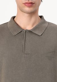 Gray ribbed polo shirt featuring a classic collar, button placket, and subtle logo on the chest. Fabric has a smooth texture.