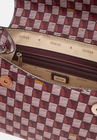 Red and white checkered pattern handbag with gold hardware and a zippered interior pocket. Lined with beige fabric featuring "GUESS" logo.