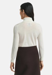 Weißes, langärmliges Poloshirt mit einem hohen Kragen und fein gestrickter Textur. Mit einem subtilen Rückendesign und kombiniert mit einem dunkelbraunen Rock.