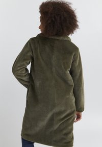 Grön fleecejacka med krage, långa ärmar och rak skärning. Texturen verkar mjuk och bekväm, och går ner till mitten av låret.