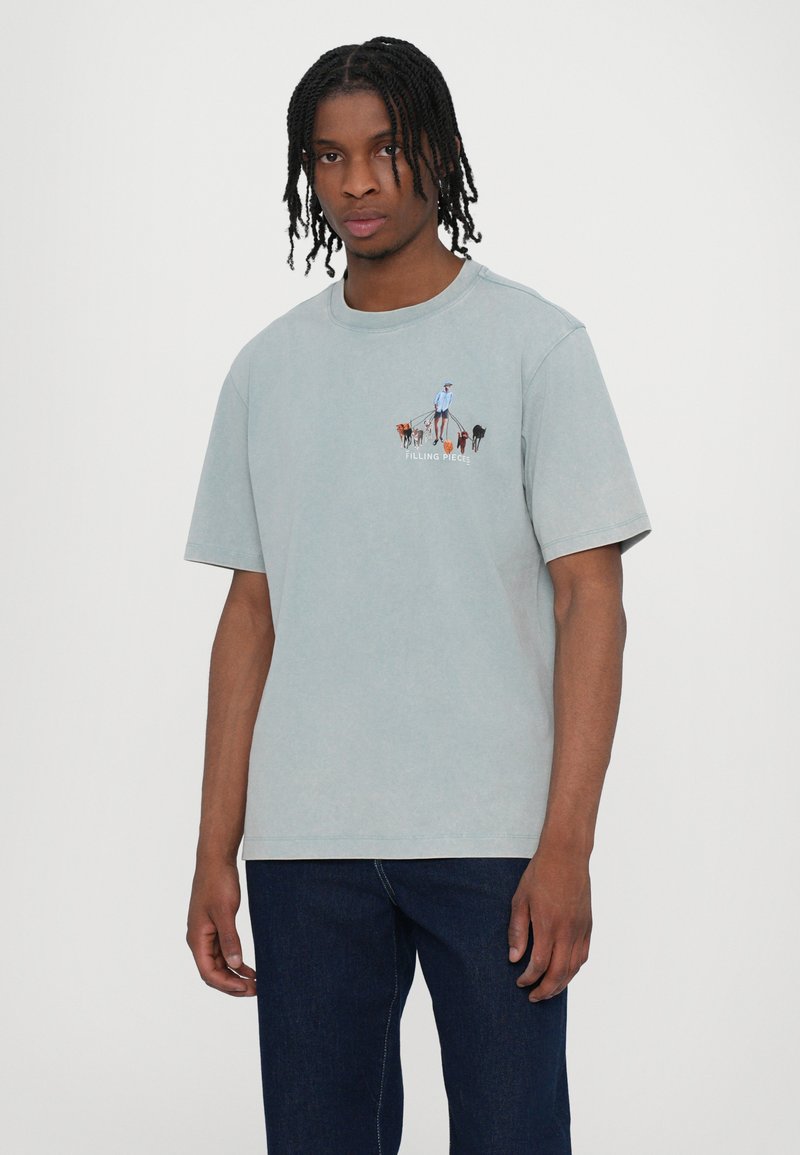 T-shirt di cotone azzurro chiaro con maniche corte, caratterizzato da una stampa che raffigura una figura che porta a passeggio dei cani sul petto. Vestibilità rilassata e foro morbido.