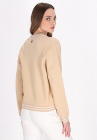 Beige gebreide trui met ribbelrand, met een ronde halslijn en witte strepen bij de manchetten en onderkant, die een eenvoudig ontwerp toont.