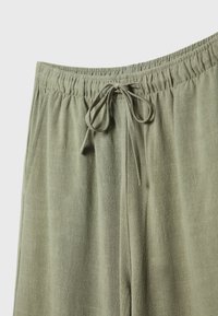 Pantalons vert olive clair avec une taille élastique, un cordon de serrage et un motif texturé subtil. Comprend des poches latérales.