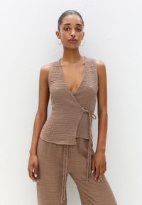 Brun, texturerad wrap-top med djup V-ringning och sidband, tillsammans med löst sittande matchande byxor, båda i en koordinerad färg.