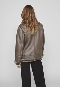 Giacca in shearling marrone con finitura testurizzata, spalle larghe, polsini in shearling a contrasto e orlo corto.