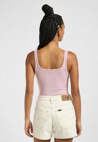 Ribbede rosa tanktop med brede stropper, parret med højtaljede kremfarvede shorts med et læder Lee-patch og syede baglommer.