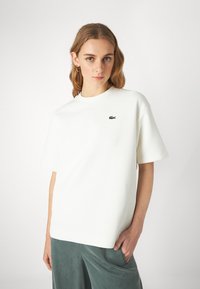 T-shirt bianco a maniche corte realizzato in tessuto testurizzato, con un piccolo logo verde ricamato sul petto. Fit rilassato e scollo rotondo.