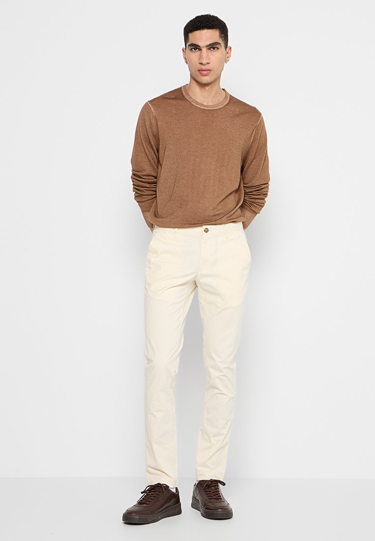 Chemise marron à manches longues, pantalon crème et baskets marron. La chemise a un col rond ; le pantalon comporte une fermeture à bouton.