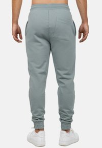 Lichtgrijze joggers met geribbelde broekspijpen en zijzakken, met een achterzak. Gecombineerd met witte sneakers.